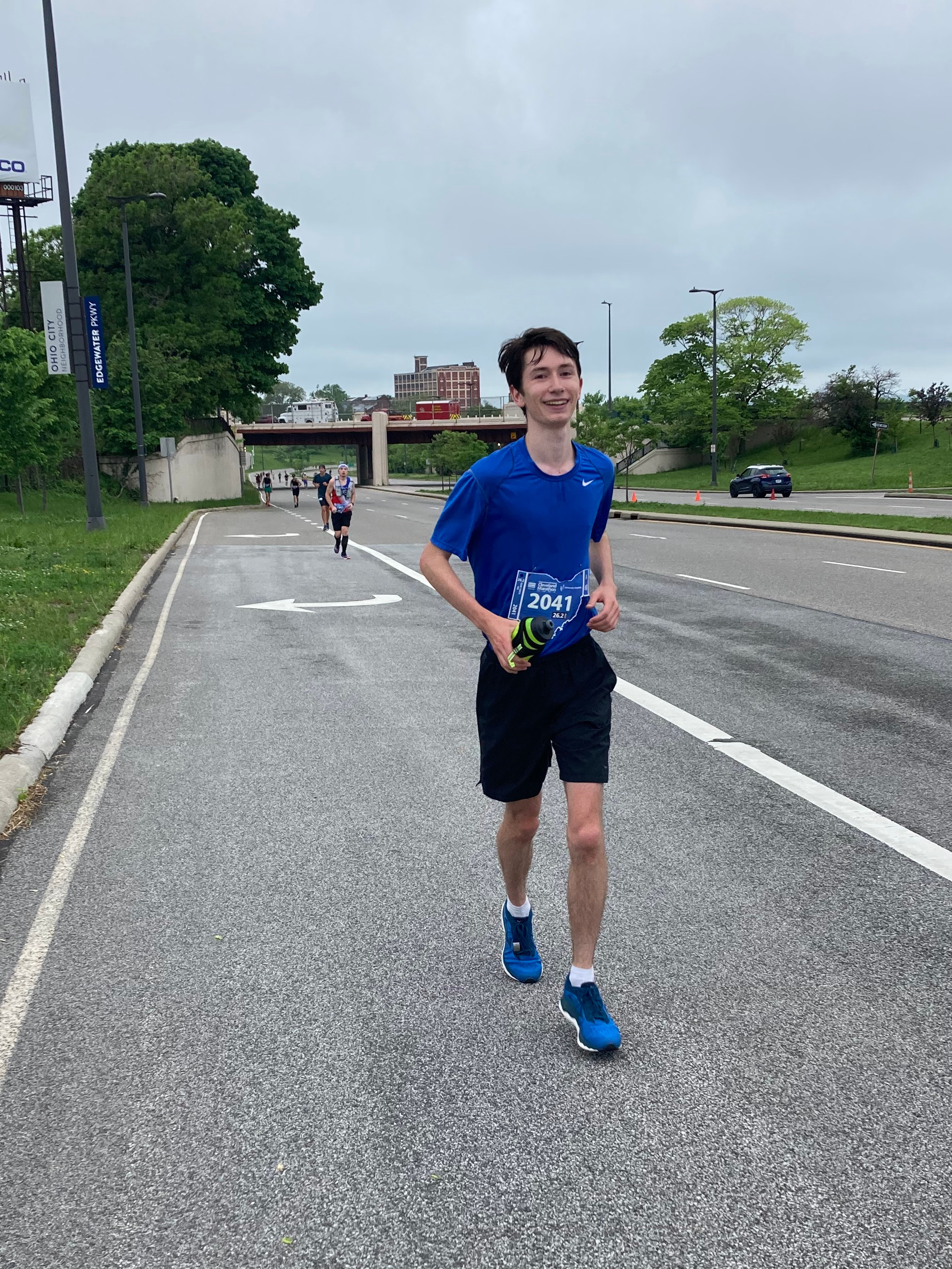 Me, running up a slight incline in a blue shirt and carrying a yellow water bottle. I'm disheveled smiling.