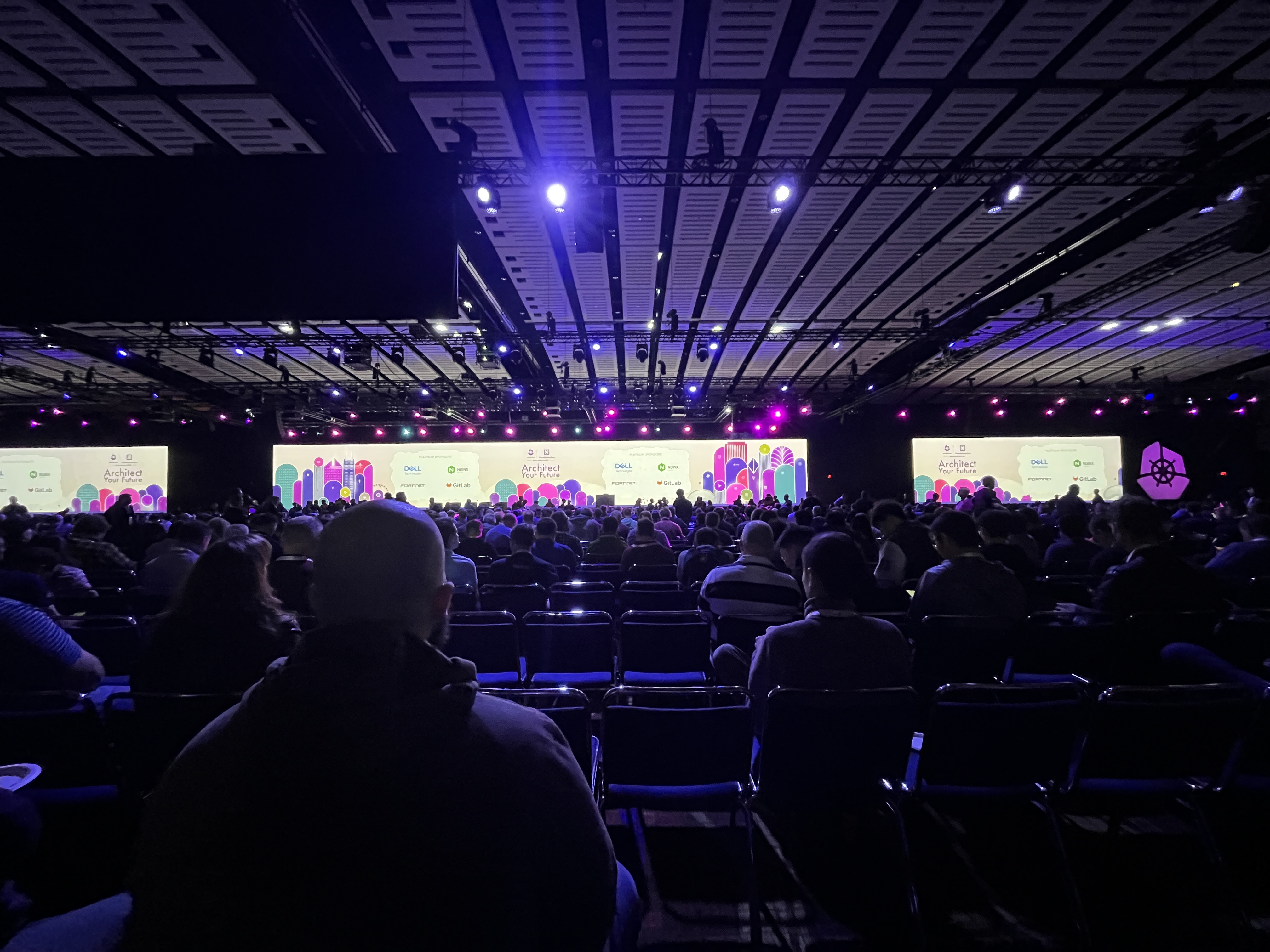 The stage in a large conference auditorium with purple and pink lights and KubeCon 2023 insignia.