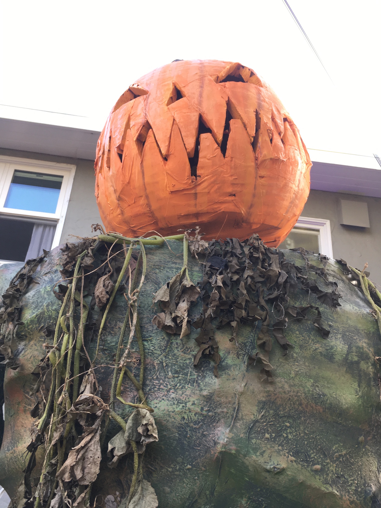 Painted Pumpkin Man draped in a mix of real and fake greenery