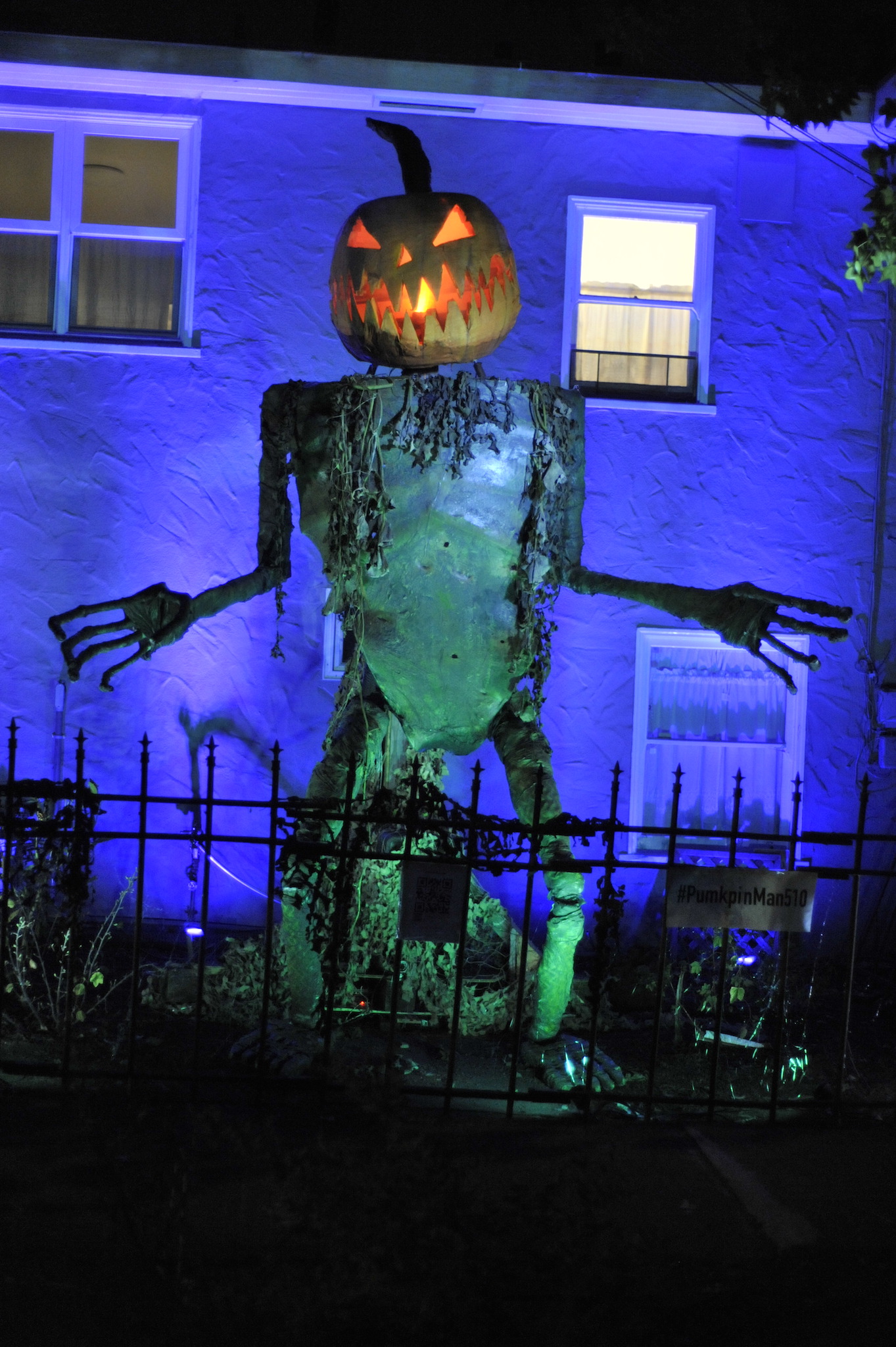 Pumpkin Man standing up with raised arm and open, glowing mouth, bathed in green light against a purple background