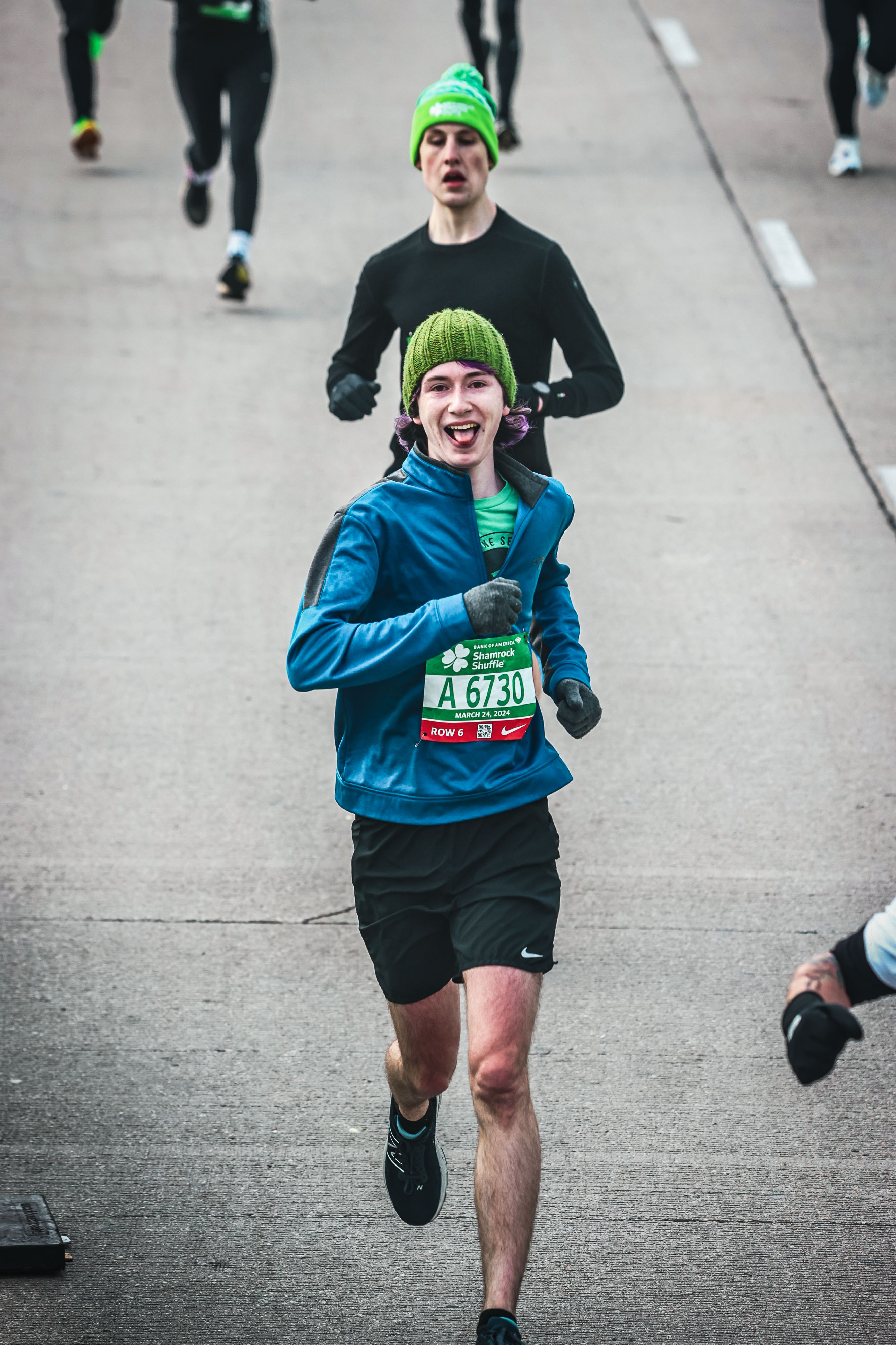 Me running across the finish line with a blue jacket and a green knit hat. My tongue is sticking out.